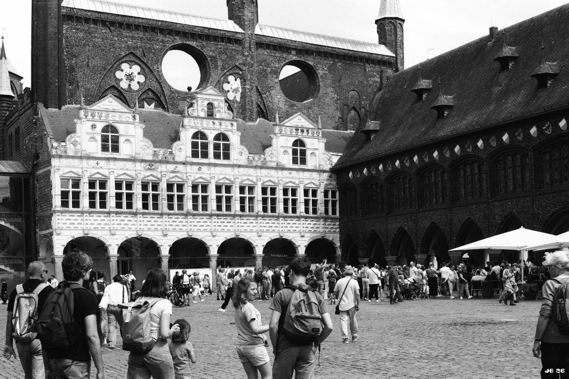 Schwarzweißfoto mit schrägem Blick auf das mittelalterliche Rathaus der Hansestadt Lübeck, ein Meisterwerk der Backsteingotik. Auf dem Platz davor halten sich viele Leute auf. Leica R4 mit 50 mm Summilux auf Foma 200-Film.